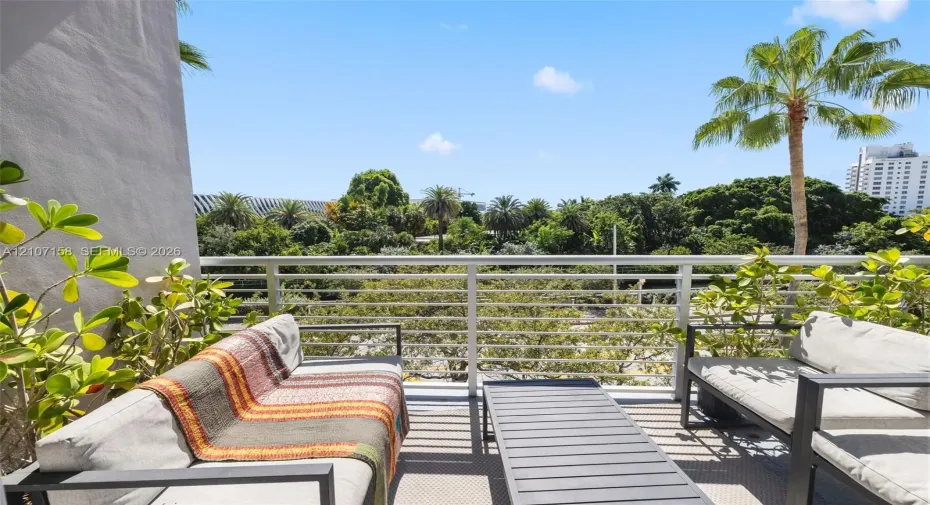 Private balcony featuring horizontal metal railing and mature tropical greenery