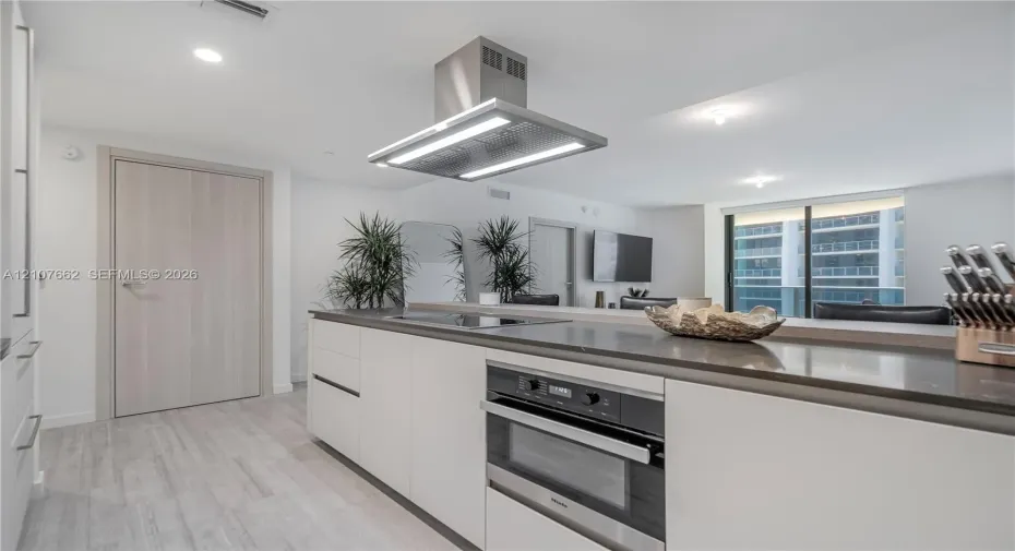 Kitchen featuring a central island with a solid-surface countertop, integrated stainless steel oven, recessed lighting, and a stainless steel ceiling-mounted range hood, complemented by light-toned wood-finish flooring