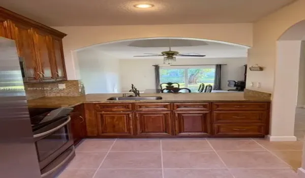 Kitchen featuring medium-toned wood cabinetry, stone countertops, stainless steel appliances, recessed ceiling lighting, and tile flooring