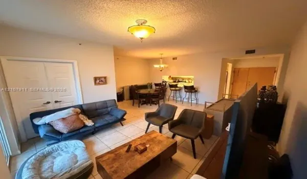 Open-concept interior featuring neutral tile flooring, dual-light ceiling fixtures, and a kitchen pass-through window with an integrated breakfast bar