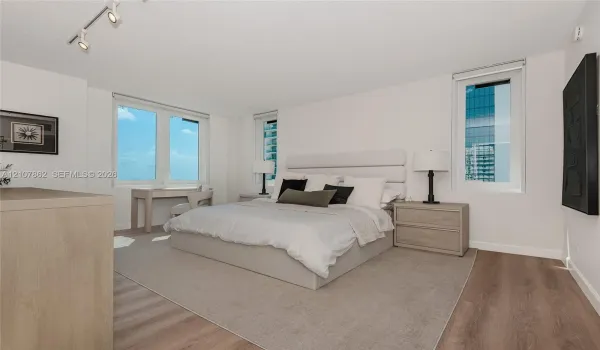 Room featuring wood-finish flooring, three windows with exterior urban scenery, and adjustable track lighting