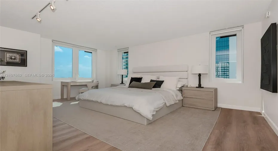 Room featuring wood-finish flooring, three windows with exterior urban scenery, and adjustable track lighting