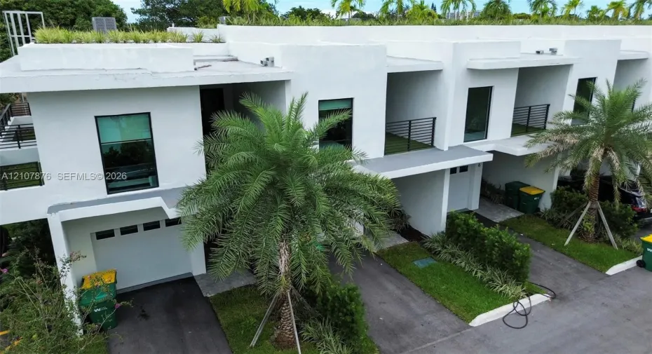 Modern architectural exterior featuring white stucco facade, second-story balconies with horizontal railing, private garages, and integrated rooftop landscaping