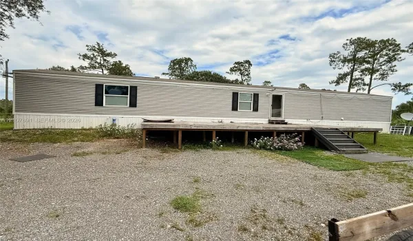 Single-story exterior with light gray horizontal siding, black shutter accents, and a raised wooden deck with integrated steps