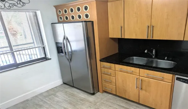 Kitchen featuring light wood-finish cabinetry, dark solid-surface countertops, dual-basin stainless steel sink with pull-down faucet, stainless steel side-by-side refrigerator, and tile flooring
