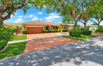 Single-story residence featuring a tiled roof, expansive paved driveway, multi-car garage, and established landscaping with mature trees