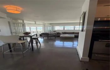 Open-concept floor plan featuring polished concrete flooring, multi-pane French doors, expansive windows with exterior scenery, and integrated stainless steel kitchen appliances