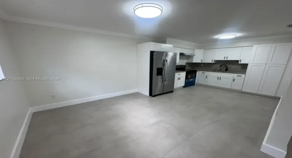 Kitchen featuring white shaker-style cabinetry, stainless steel side-by-side refrigerator, stone-composite countertops, matte black gooseneck faucet, and large-format tile flooring