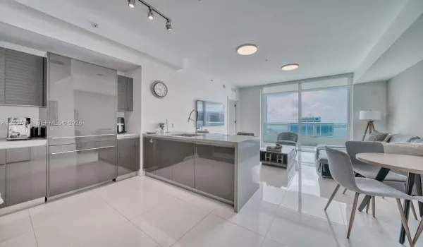 Modern kitchen featuring high-gloss cabinetry, a central island with a waterfall countertop, integrated stainless steel refrigerator, porcelain tile flooring, and floor-to-ceiling glass doors