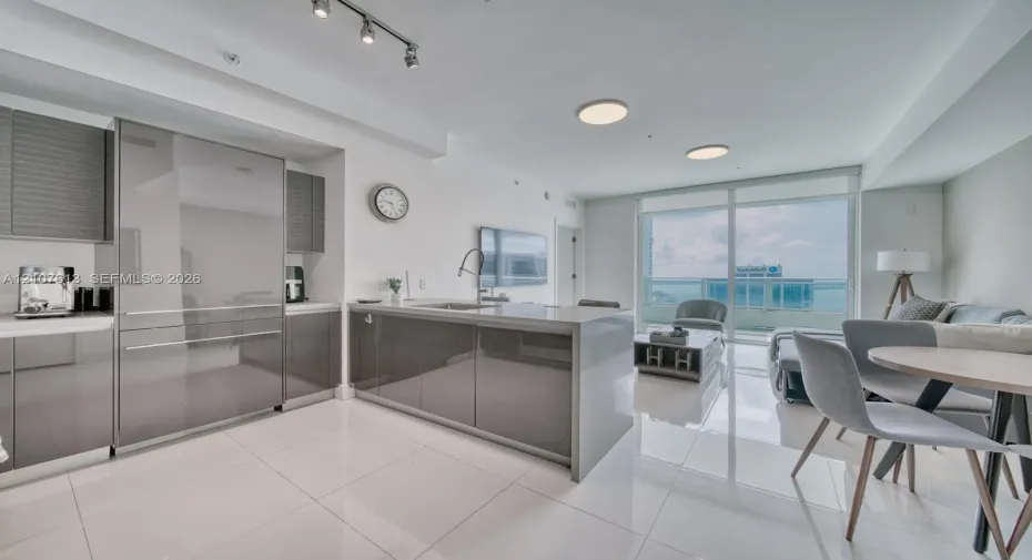 Modern kitchen featuring high-gloss cabinetry, a central island with a waterfall countertop, integrated stainless steel refrigerator, porcelain tile flooring, and floor-to-ceiling glass doors