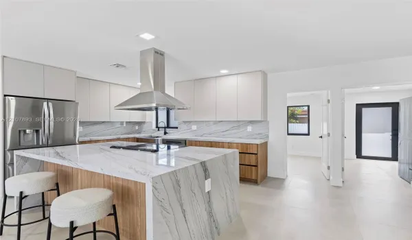 Kitchen featuring a waterfall island with stone countertop, wood-finish cabinetry, stainless steel appliances, a stainless steel range hood, and tile flooring