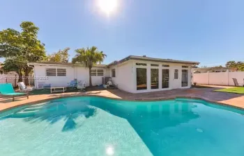 In-ground pool with stone paver surround, expansive patio space, white exterior siding, and custom glass-panel entry door