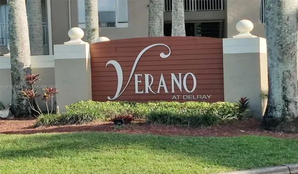Community monument sign featuring horizontal wood-slat siding, decorative concrete pillars with ball finials, and professional landscaping