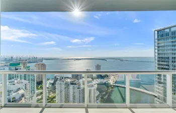 Covered balcony with a glass-panel railing, tile flooring, and expansive water and urban skyline backdrop
