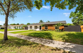 Single-story residence featuring a mid-century modern aesthetic, wood-panel siding, white stucco exterior, asphalt shingle roof, and a black privacy fence