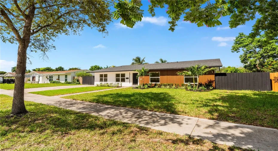 Single-story residence featuring a mid-century modern aesthetic, wood-panel siding, white stucco exterior, asphalt shingle roof, and a black privacy fence