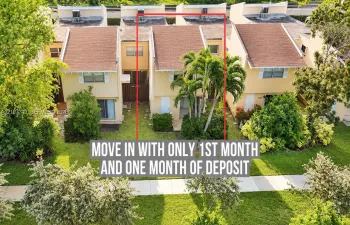 Two-story townhome exterior featuring a pitched roof, neutral stucco siding, sliding glass doors, and mature palm tree landscaping