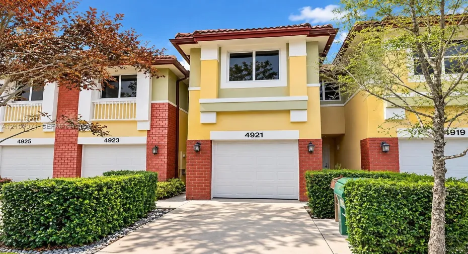Multi-story townhouse exterior featuring a concrete driveway, integrated single-car garage, brick facade accents, and clay tile roofing