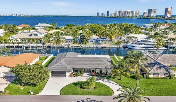 Waterfront single-story residence featuring a tile roof, concrete circular driveway, manicured lawn, and mature palm trees