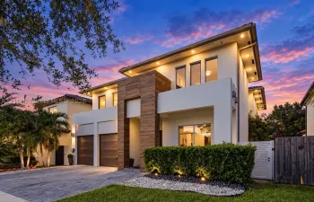 Contemporary exterior featuring smooth stucco finish, vertical wood-paneling accents, recessed soffit lighting, two-car garage with wood-finish doors, and paved driveway