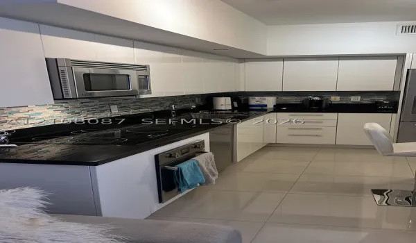Kitchen featuring high-gloss white cabinetry, polished dark stone countertops, linear glass mosaic tile backsplash, integrated stainless steel appliances, and large-format tile flooring