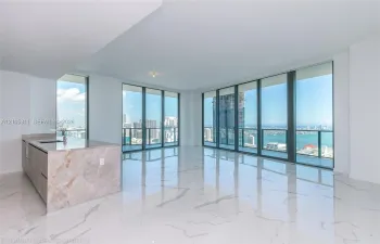 Expansive floor-to-ceiling windows, large format marble-look tile flooring, and a kitchen island with a stone countertop and integrated sink