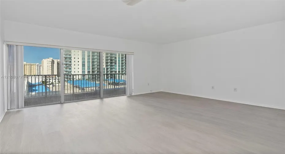 Open-concept interior featuring light wood-finish flooring, sliding glass balcony doors, and a metal-railed balcony