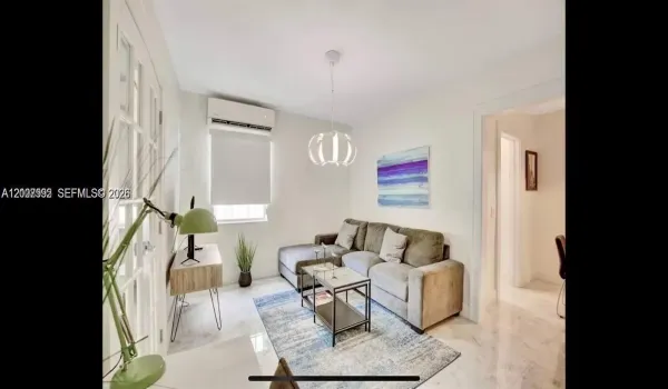 Living area featuring light-toned tile flooring, recessed ceiling lighting, a wall-mounted climate control unit, and French doors