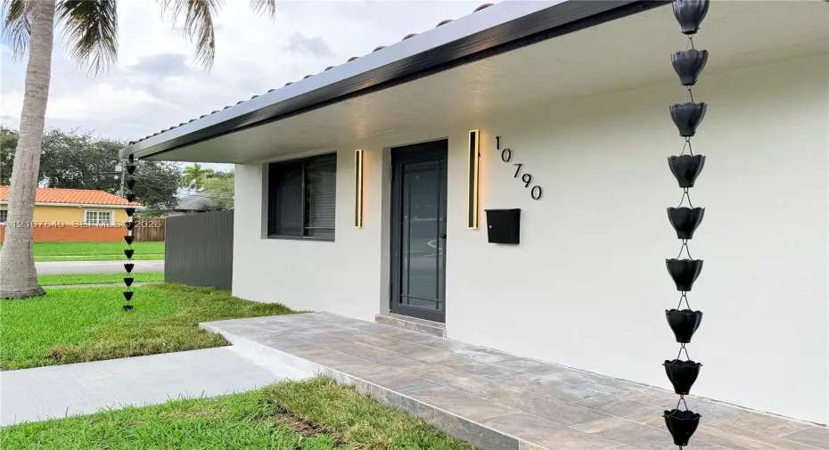 Exterior featuring a clean white facade, tiled porch entry, sleek vertical wall-mounted lighting, and matte black rain chains