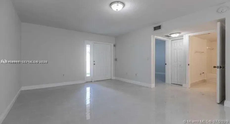 Neutral-toned interior featuring glossy tile flooring, recessed and flush-mount lighting, a six-panel exterior door with sidelight, and a walk-in closet with six-panel double doors