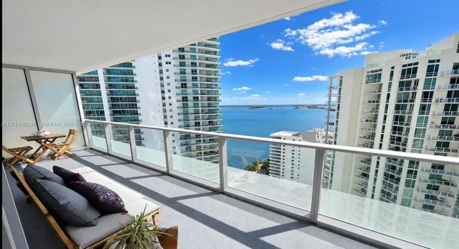 Private balcony featuring a glass-panel railing, concrete flooring, and water scenery