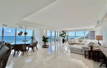Open-concept interior featuring large-format stone flooring, floor-to-ceiling glass walls, recessed lighting, and modern pendant fixtures