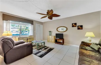 Neutral-toned interior featuring oversized tile flooring, a large window with a built-in cornice, and a ceiling fan with decorative leaf-shaped blades