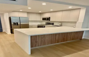Kitchen featuring flat-panel cabinetry, light-toned stone-finish countertops, wood-finish island paneling, recessed lighting, and stainless steel appliances