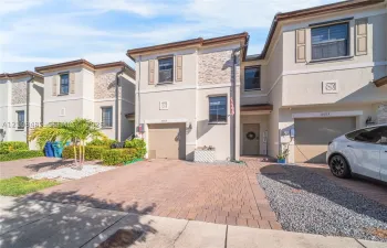 Stucco exterior featuring stacked stone accents, paved driveway, attached garage, and decorative exterior shutters