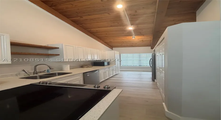 Vaulted ceiling with exposed wood planking, white cabinetry, integrated track lighting, wood-finish flooring, and solid-surface countertops