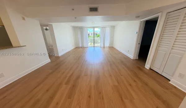 Open-concept interior featuring wood-finish flooring, louvered closet doors, and a glass-paneled sliding door opening to a balcony