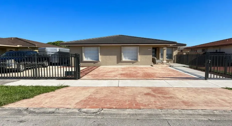 Single-story residence featuring a low-slope roof, stucco exterior, stamped concrete driveway, and a metal perimeter fence