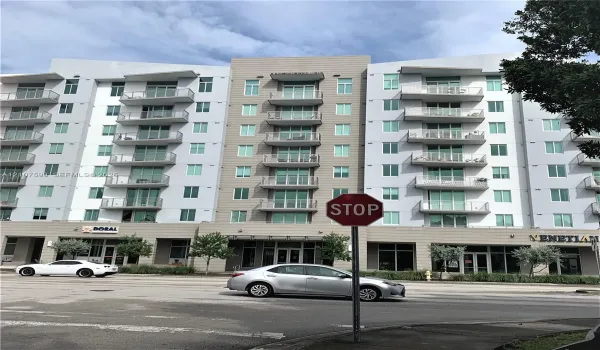 Multi-story building exterior featuring a mixed-material facade, private glass-railed balconies, and ground-level commercial storefronts