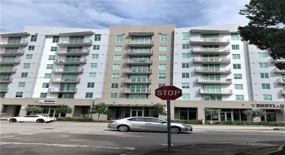 Multi-story building exterior featuring a mixed-material facade, private glass-railed balconies, and ground-level commercial storefronts