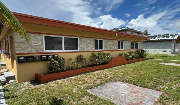 Exterior facade featuring multi-tone stucco finish, natural stacked stone veneer accents, integrated brick planter boxes, and a series of wall-mounted metal mailboxes