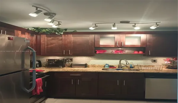Dark wood cabinetry featuring brushed metal hardware, stone-finish countertops, textured tile backsplash, stainless steel appliances, and dual adjustable track lighting fixtures