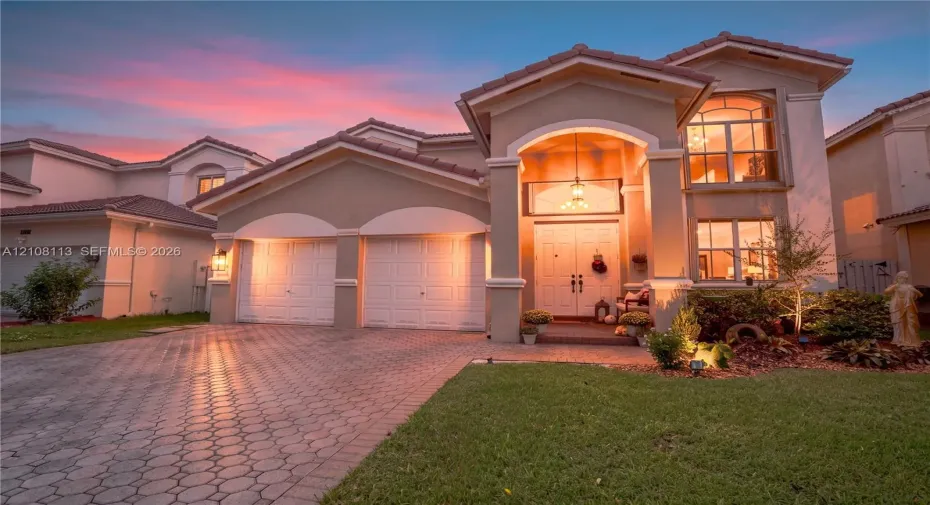 Stucco exterior featuring a dual-car garage, arched covered entryway, paver driveway, and tiled roof