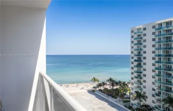 Private balcony with white metal railings, oriented toward an expansive ocean horizon and sandy shoreline