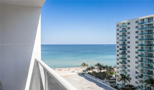 Private balcony with white metal railings, oriented toward an expansive ocean horizon and sandy shoreline