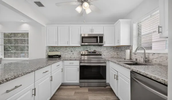 Kitchen featuring white Shaker-style cabinetry, stone-finish countertops, stainless steel appliances, a glass-tiled backsplash, and wood-finish flooring