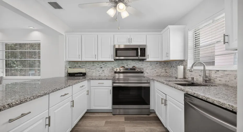 Kitchen featuring white Shaker-style cabinetry, stone-finish countertops, stainless steel appliances, a glass-tiled backsplash, and wood-finish flooring