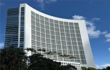 High-rise structure featuring a curved white façade, floor-to-ceiling glass windows, and stacked recessed balconies