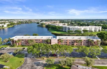 Multi-story residential building featuring stucco exterior, expansive lake frontage, mature trees, and dedicated surface parking
