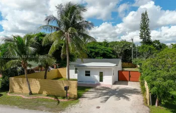 Single-story residence featuring white exterior walls, a shingled roof, a gated gravel driveway, and wood-panel privacy fencing enclosing the side yard